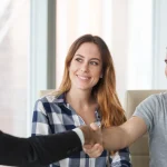 A company representative and homeowners shake hands after a roofing project
