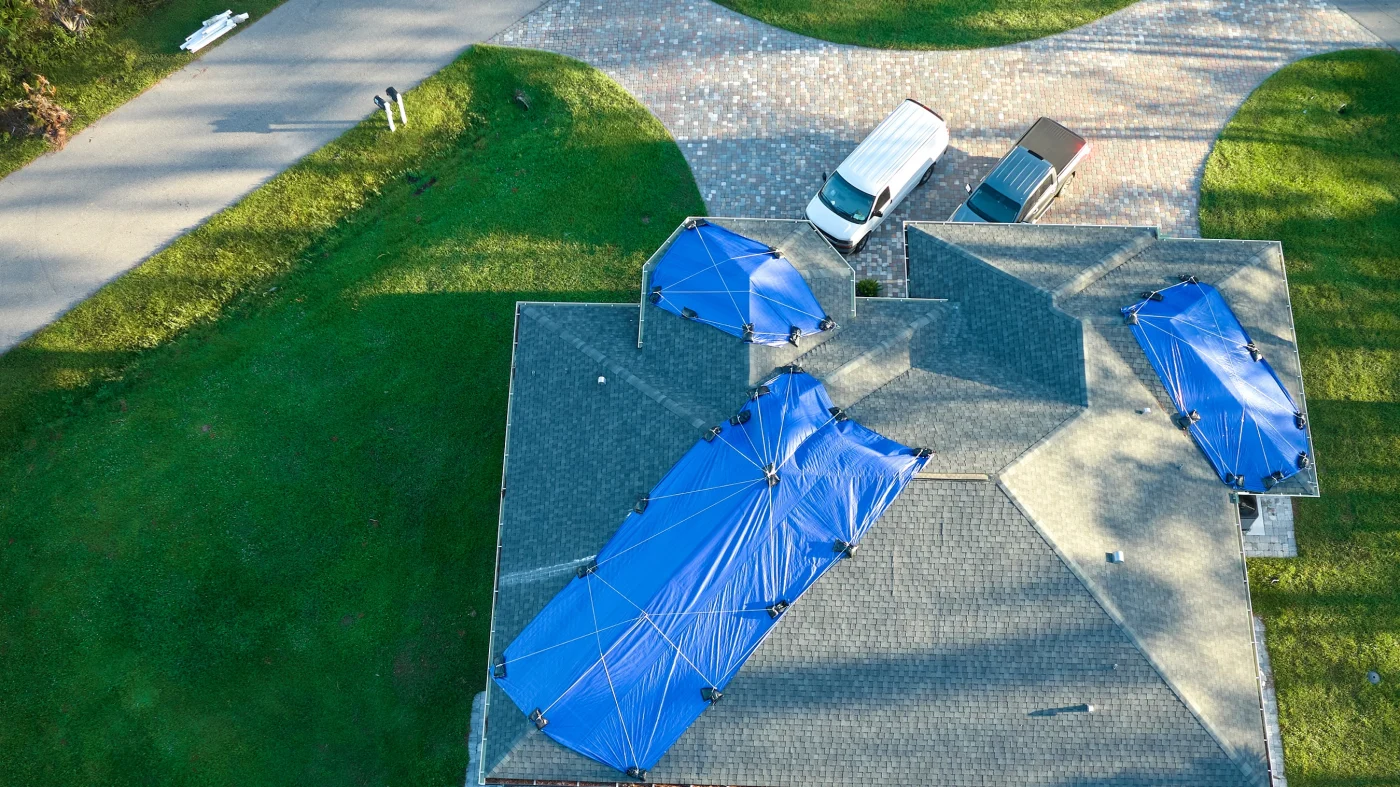 A storm-damaged roof covered with three large tarps